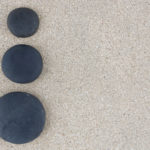 Three black zen stones at left side of sand background