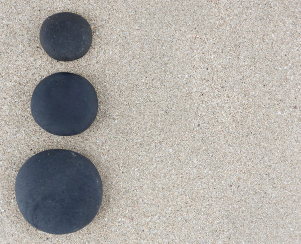 Three black zen stones at left side of sand background