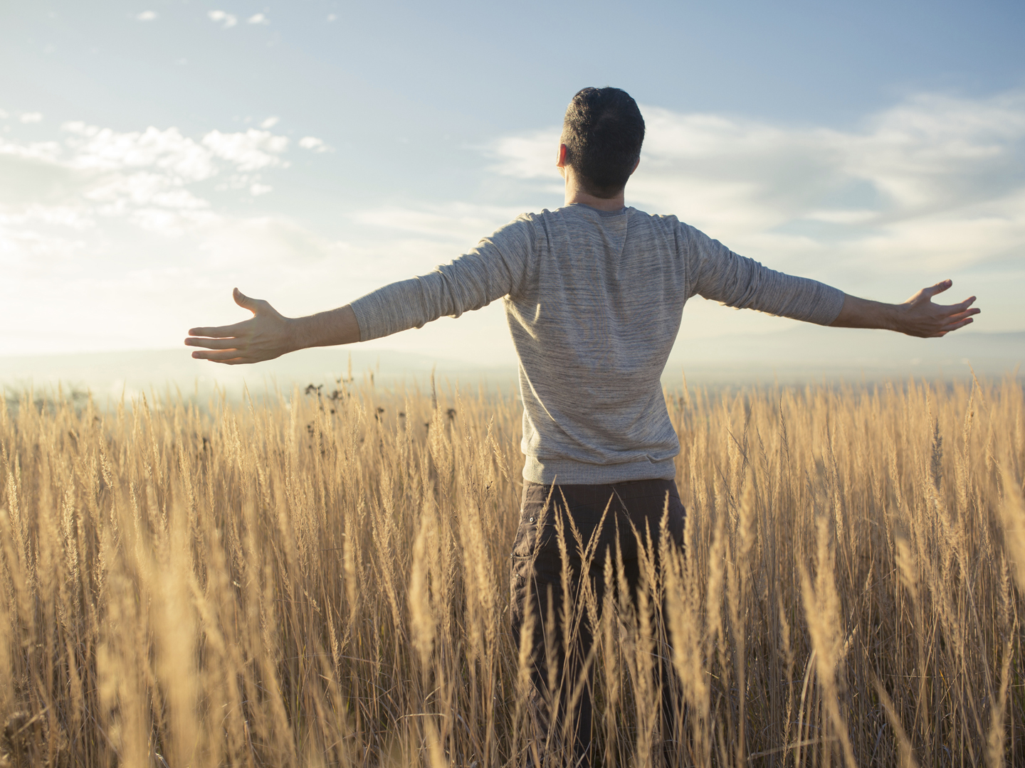 Young caucasian man standing in the middle of a prairie with his arms outstretched, enjoying a beautiful sunny day in the nature.