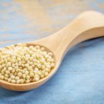 millet grain on a wooden spoon against blue painted grunge wood