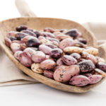 Pinto beans on wooden scoop on beige table cloth. Healthy eating, agriculture background.