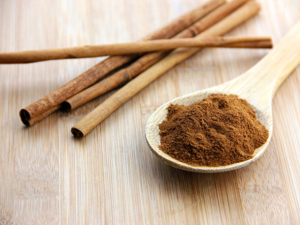A spoonful of cinnamon and cinnamon sticks set on a bamboo wooden surface