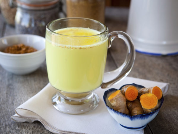 Golden milk. Turmeric herbal medicine, an anti-inflammatory. Shallow DOF, focus on the brim of the glass and the foam on milk