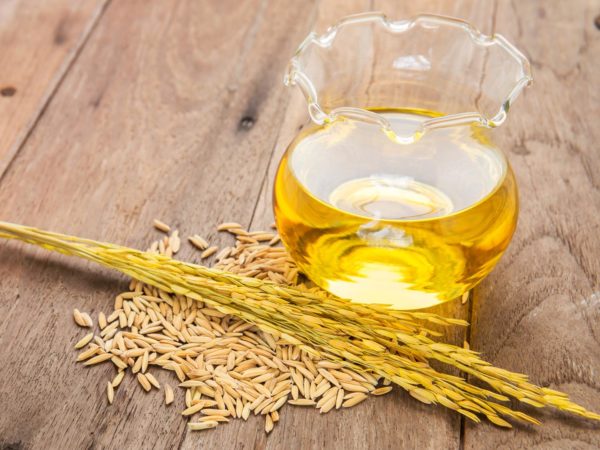 Rice bran oil in bottle glass and unmilled rice on wooden background