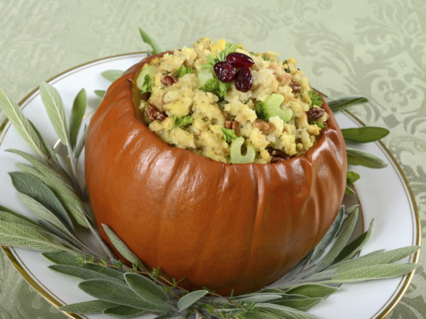 A fresh whole pumpkin baked and stuffed with savory herb dressing with bread, celery, pecans, and cranberries, perfect for Thanksgiving or other festive autumn and winter meals.