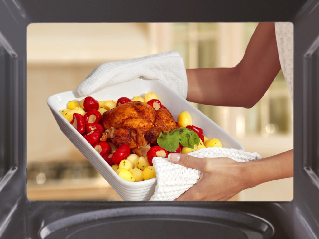 hands of woman is taking out chicken with potato from oven