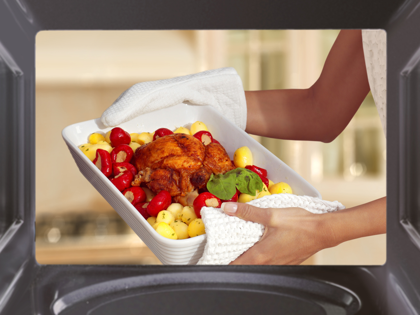 hands of woman is taking out chicken with potato from oven