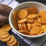 Raw sweet potato with at the vintage wooden table, in the bowl and a towel