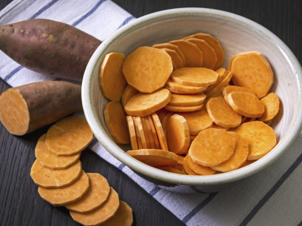 Raw sweet potato with at the vintage wooden table, in the bowl and a towel