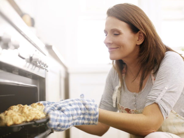 A mature woman taking scones out from the oven