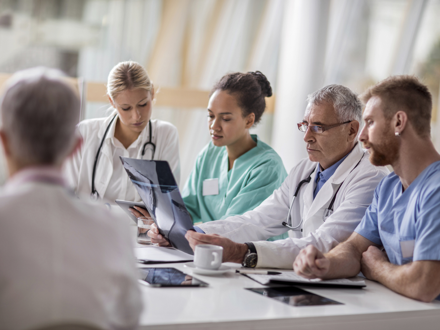 Group of multi-tasking healthcare workers working in the hospital. Focus is on senior doctor analyzing an X-ray.