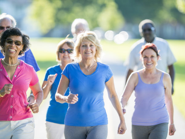 A multi-ethnic group of senior adults are exercising together by walking in the park on a sunny day.