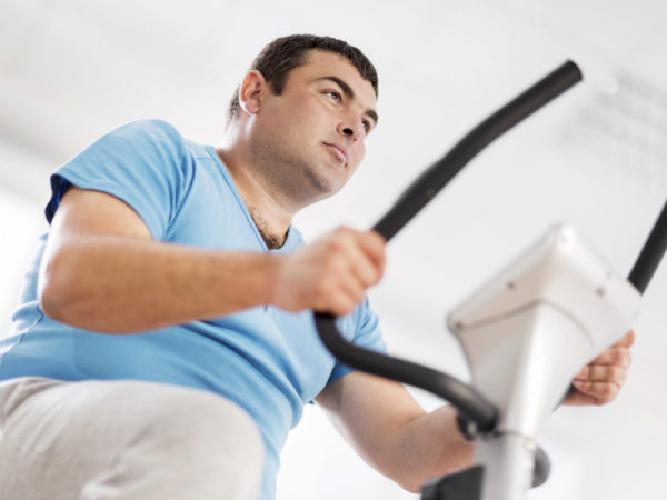 Low angle view of young serious overweight man cycling on exercise bike.