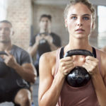 Shot of a group of people doing squats with a kettle bell in a gym