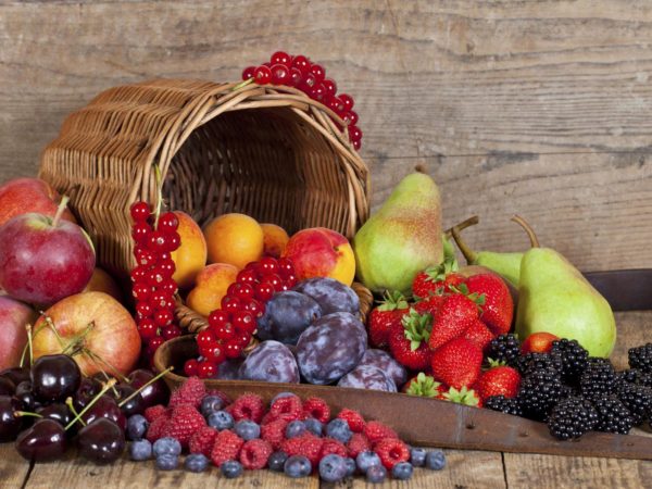 Harvested Summer Fruits and Berries an a wooden Table with its Basket.