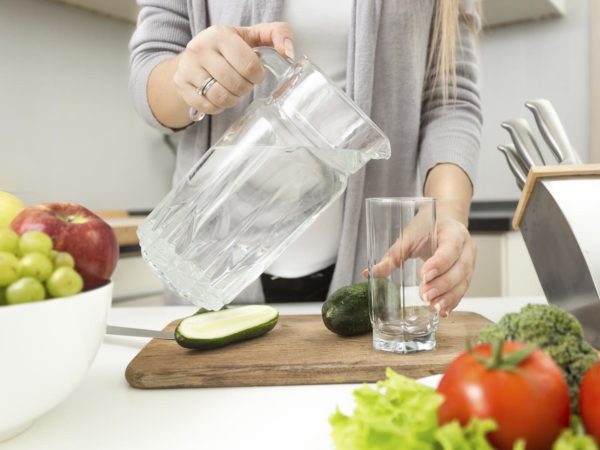 Closeup photo of woman pouring water in glass on kitchen
