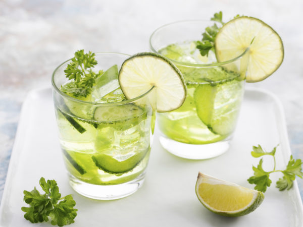 Lime, cucumber, parsley cocktail, lemonade, detox water with ice cubes in a glasses on a white plate