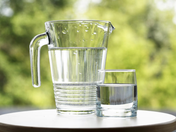 Glass of water near jug on green nature background