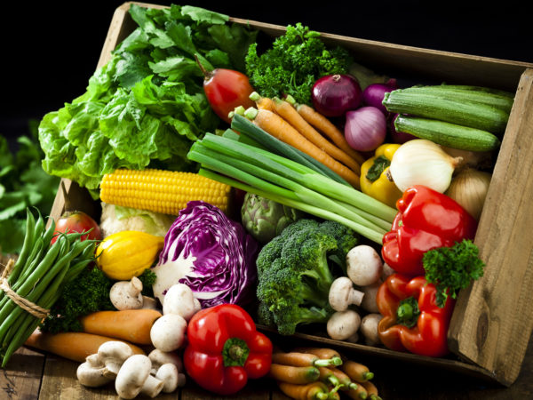 A wooden crate is filled with fresh, colorful organic vegetables. The crate is tilted and some vegetables are out of it on a rustic wood table.  DSRL studio photo taken with Canon EOS 5D Mk II and Canon EF 70-200mm f/2.8L IS II USM Telephoto Zoom Lens