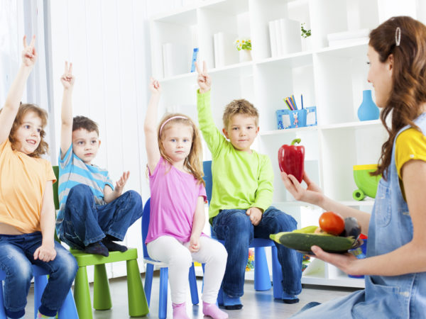 &quot;Portrait of an cute children talking about vegetable in a preschool, selective focus to children with arms raised guessing, teacher learning children about vegetable. Holding paprika.&quot;