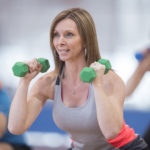 A group of adults are taking a fitness class together at the gym. They are using dumbbell weights to workout their arms.