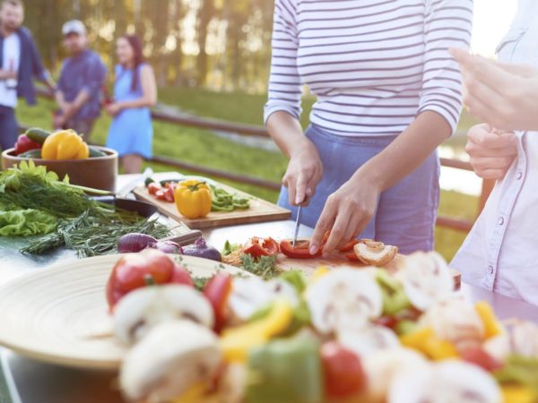 One women cutting pepper on cutting board, her friend putting food on stick