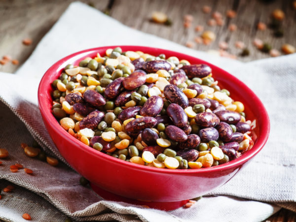 Bean mix: purple beans, green and red lentils, dry peas in a red bowl, vintage wooden background, selective focus