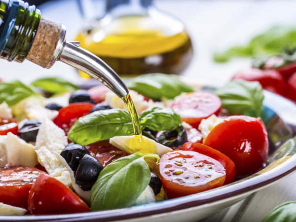 Caprese. Caprese salad. Italian salad. Mediterranean salad. Italian cuisine. Mediterranean cuisine. Tomato mozzarella basil leaves black olives and olive oil on wooden table. Recipe - Ingredients