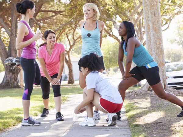 Group Of Female Runners Warming Up Before Run On Suburban Street Chatting