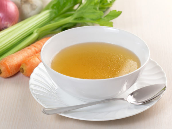 bowl of broth and fresh vegetables on wooden table