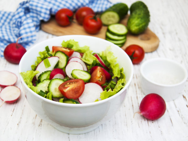 Spring salad with tomato, cucumbers and radish on a wooden background