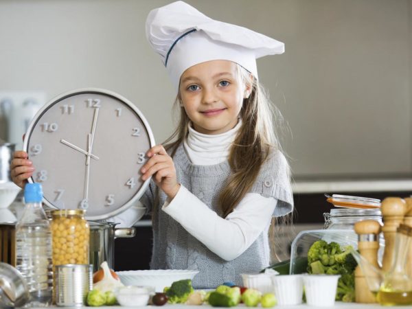 Portrait of cute little girl counting time down when cooking