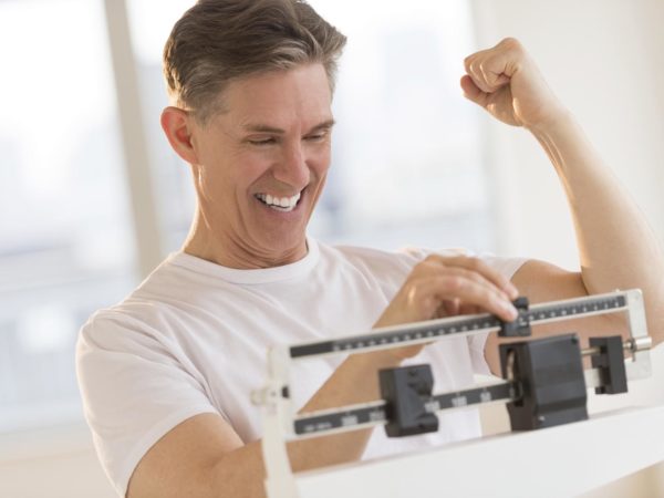 Excited mature man clenching fist while using balance weight scale at gym