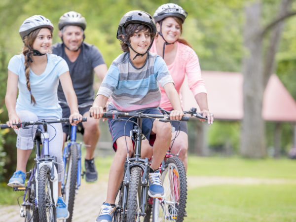 A family of four is going on a bike ride together through the park on a beautiful sunny day.