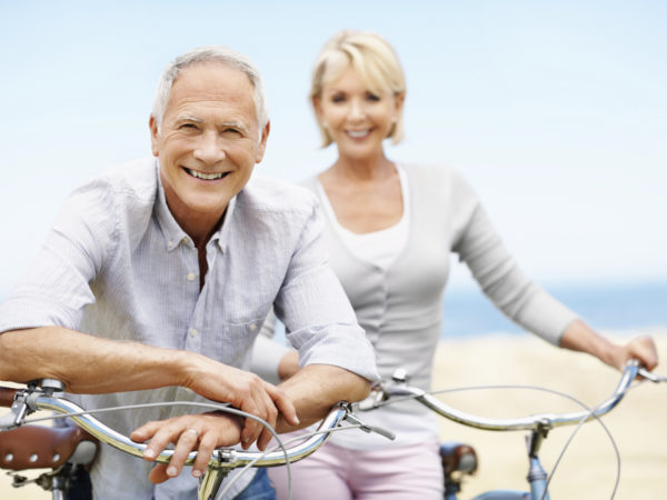 A mature man leaning on his bikes handlebars while a mature woman smiles in the background-copyspace