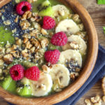Healthy breakfast green smoothie bowl topped with fruits, nuts, berries and seeds over wooden background close up