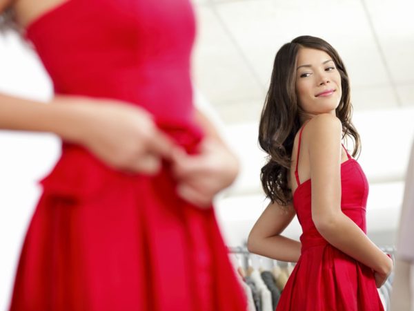 Girl trying dress in looking in mirror cheerful and happy. Cute beautiful mixed race Asian / Caucasian young woman oin red dress.