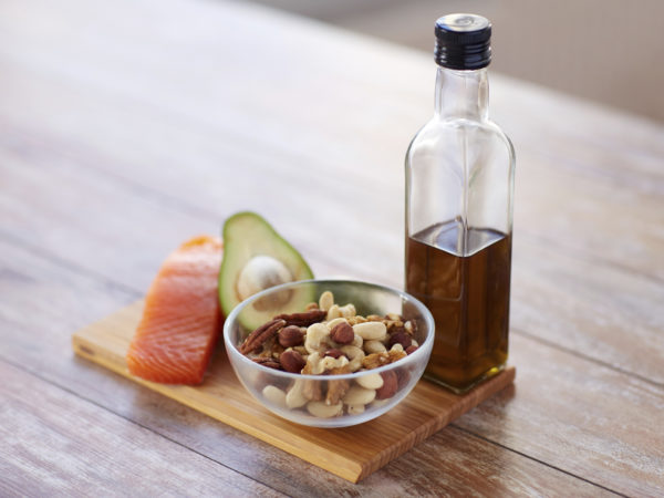healthy eating, diet and culinary concept - close up of salmon fillets, avocado, olive oil bottle and nuts in glass bowl on table