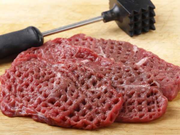 Three raw minute steaks displayed next to a meat mallet after being pounded and tenderised