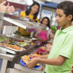 Middle school students getting lunch items in cafeteria line.