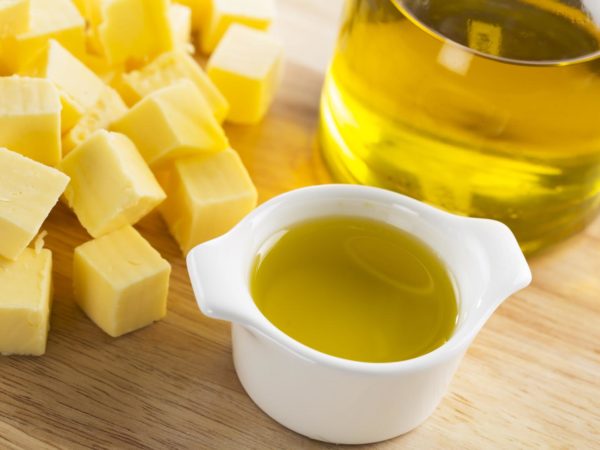 Olive oil in small glass container with bottle of oil and cubes of butter