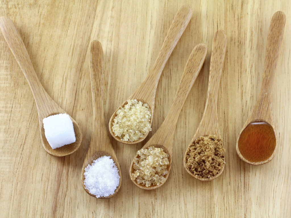 Spoons of different types of sugar on the wooden background