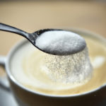 Sprinkling refined sugar from a spoon into a cup of coffee