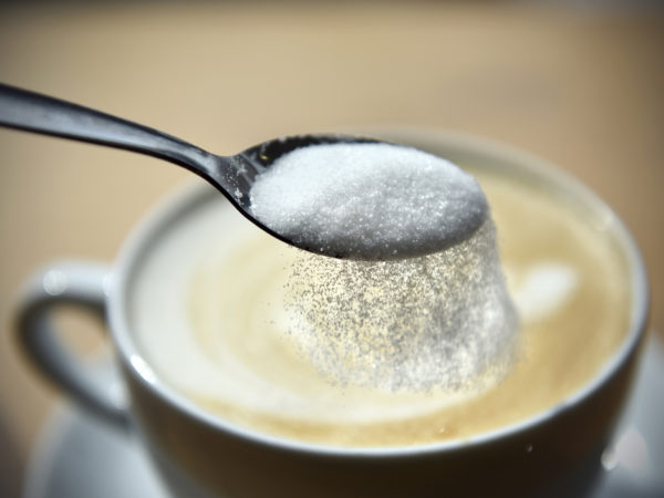 Sprinkling refined sugar from a spoon into a cup of coffee