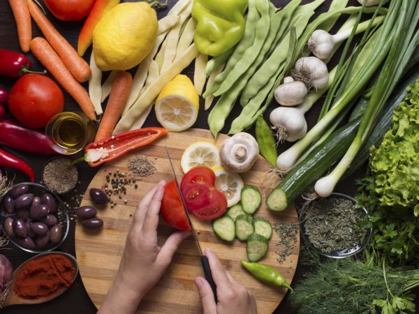 Human hands cutting raw vegetables on a cutting board and vegetables and spices around