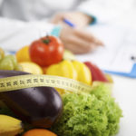 Healthy nutrition concept. Close-up of fresh vegetables and fruits with measuring tape lying on doctor&#039;s desk.