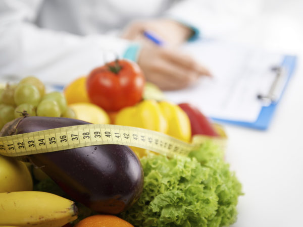Healthy nutrition concept. Close-up of fresh vegetables and fruits with measuring tape lying on doctor&#039;s desk.