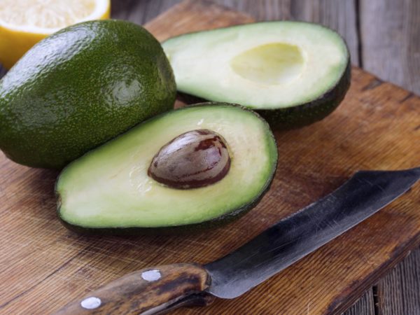 Sliced avocado and knife on old cutting board. Guacamole ingredients.