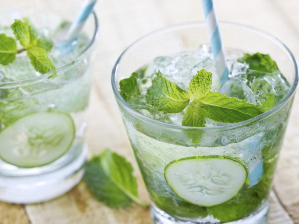 glass of cold water with fresh mint leaves and cucumber with ice cubes on wooden background