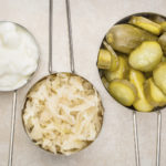 sauerkraut, cucumber pickles and yogurt - popular probiotic fermented food - three measuring cups against ceramic tile